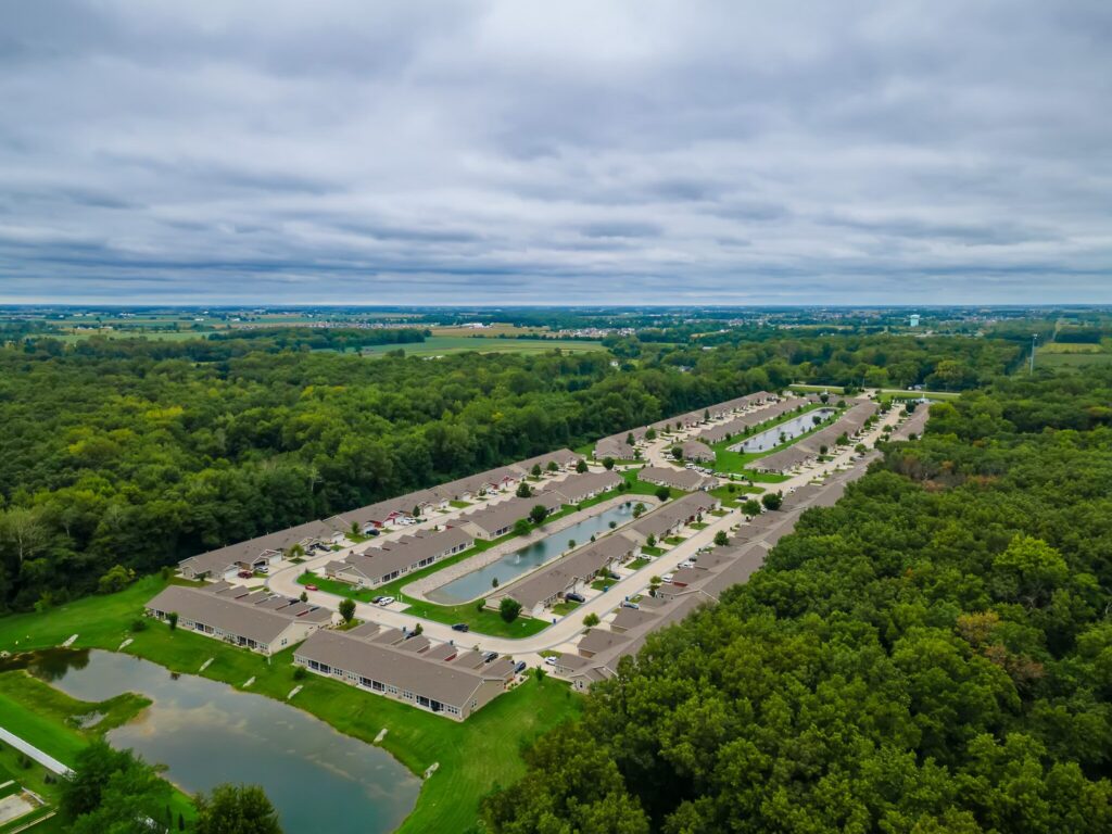 Aerial view of a residential neighborhood with rows of homes, ponds, and surrounding green trees under a cloudy sky.