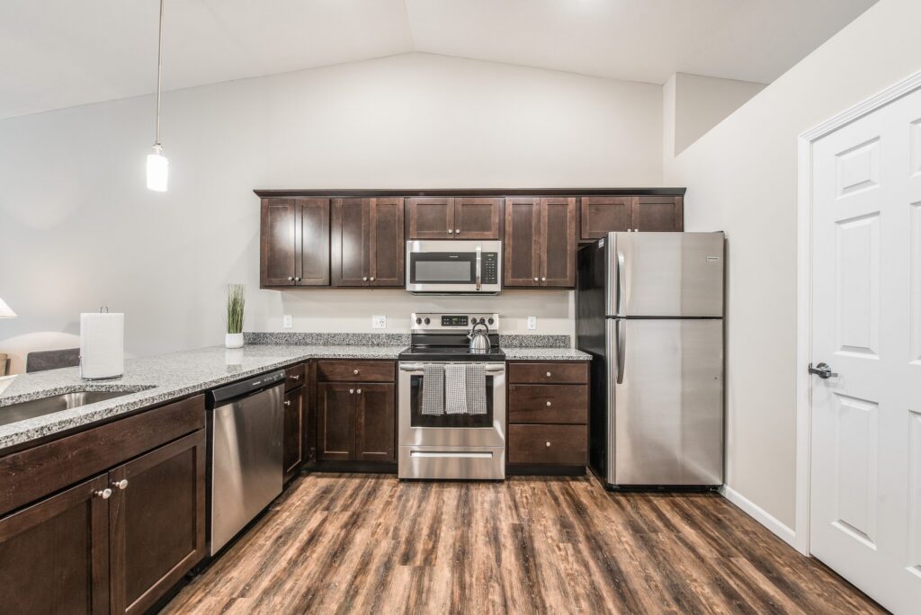 Modern kitchen with stainless steel appliances, dark wood cabinets, granite countertops, and wood-style flooring.