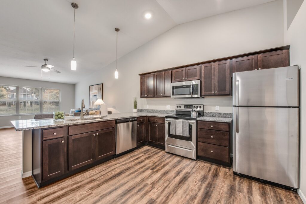 Modern kitchen with dark wood cabinets, stainless steel appliances, granite countertops, and wood flooring, open to a living area with large windows.