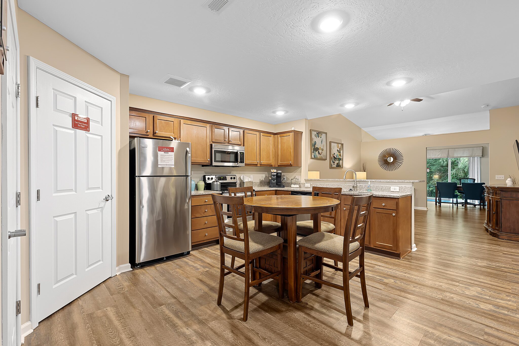 Modern open-concept kitchen and dining area with stainless steel appliances, wooden cabinets, round table with four chairs, and view into the living room.