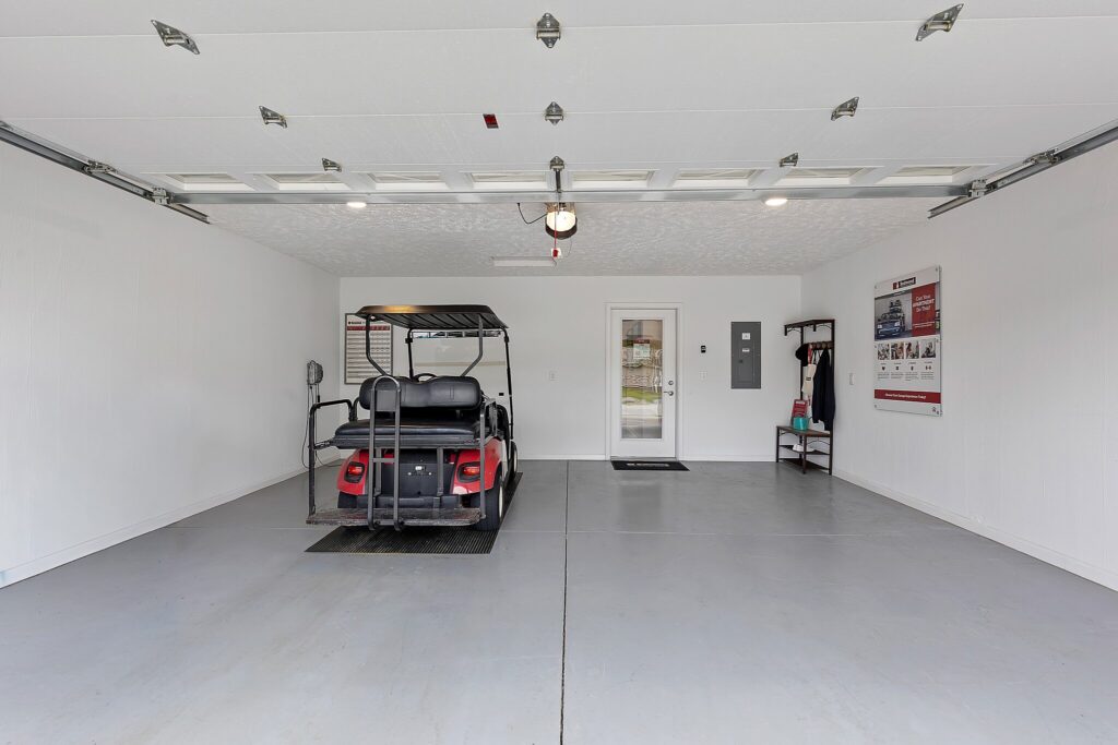 A clean, spacious garage with a single golf cart parked inside, white walls, a closed side door, and a wall-mounted rack and poster.