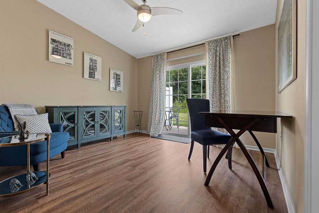 Home office with a wooden desk and blue chair near sliding glass doors, blue upholstered chair, sideboard, wall art, and wood flooring.