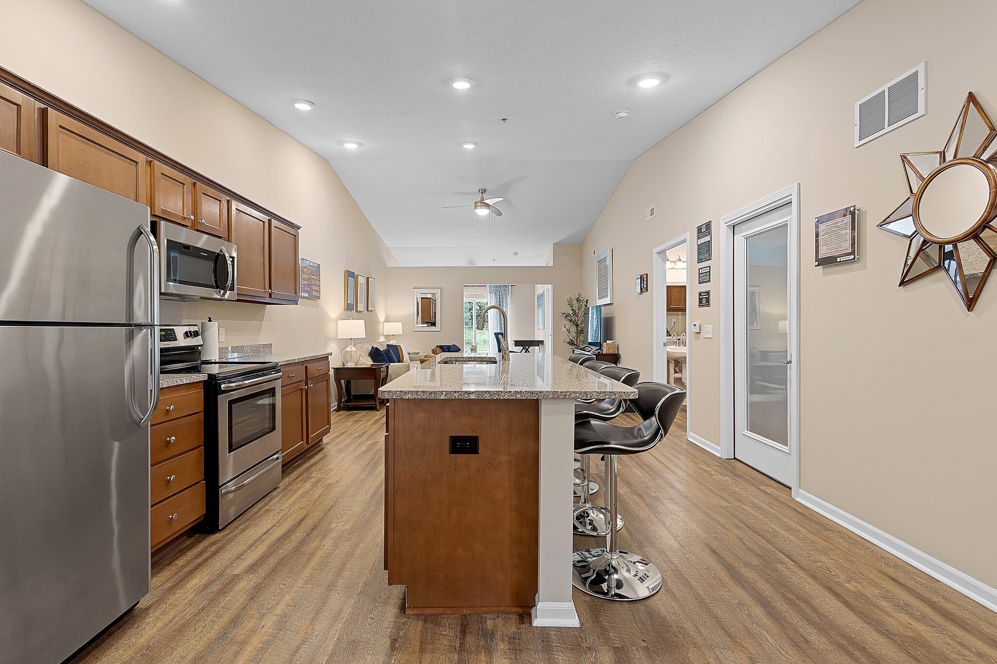 Open-concept kitchen and living area featuring stainless steel appliances, wooden cabinets, a center island with bar stools, and hardwood flooring.