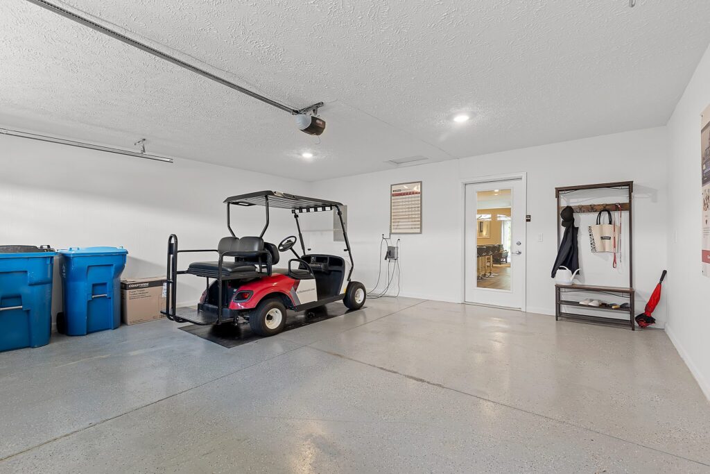 A clean garage with a red golf cart, two blue recycling bins, a coat rack, and a door leading to the interior of the house.