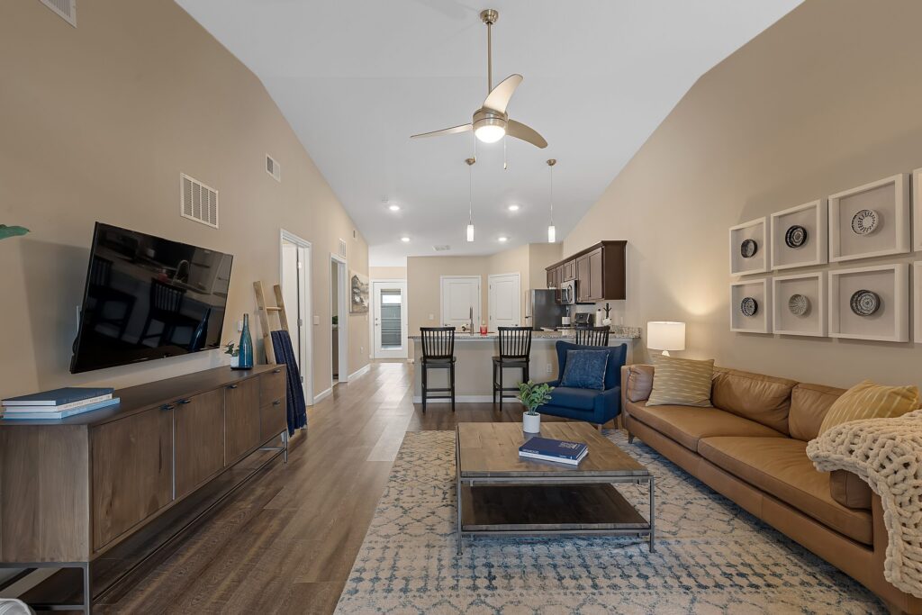 Modern open-concept living room and kitchen with brown leather sofa, wall-mounted TV, dining area, and neutral decor in warm tones.