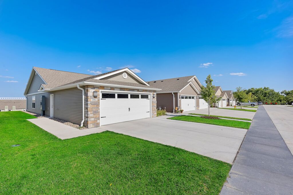 Single-story suburban homes with attached garages, neatly mowed lawns, and a clean concrete driveway on a clear, sunny day.
