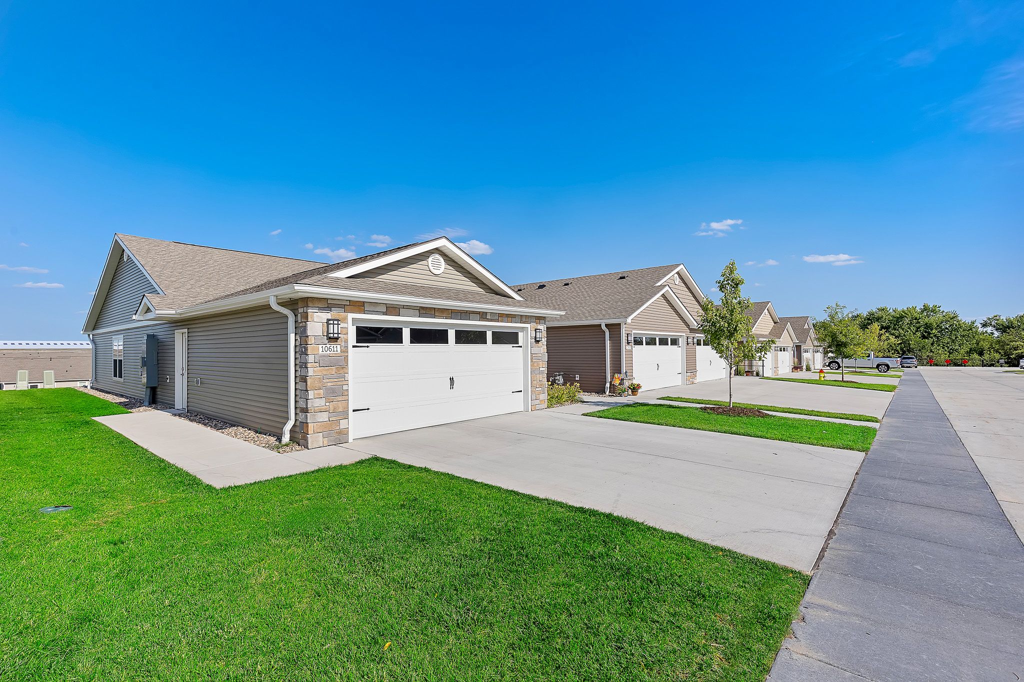 Single-story suburban homes with attached garages, neatly mowed lawns, and a clean concrete driveway on a clear, sunny day.