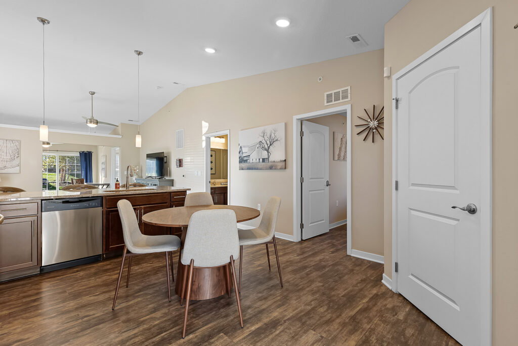 Modern kitchen and dining area with wood floors, round table with four chairs, stainless appliances, neutral walls, and decorative art on the walls.