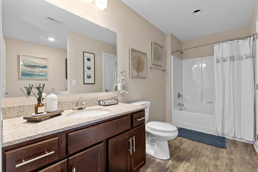 Modern bathroom with a single sink vanity, granite countertop, toilet, bathtub with shower and curtain, wall art, and wood-style flooring.