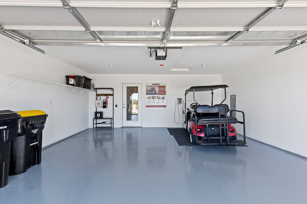 Open garage with a golf cart parked on the right, storage bins and shelves on the left, and two garbage bins in the foreground.
