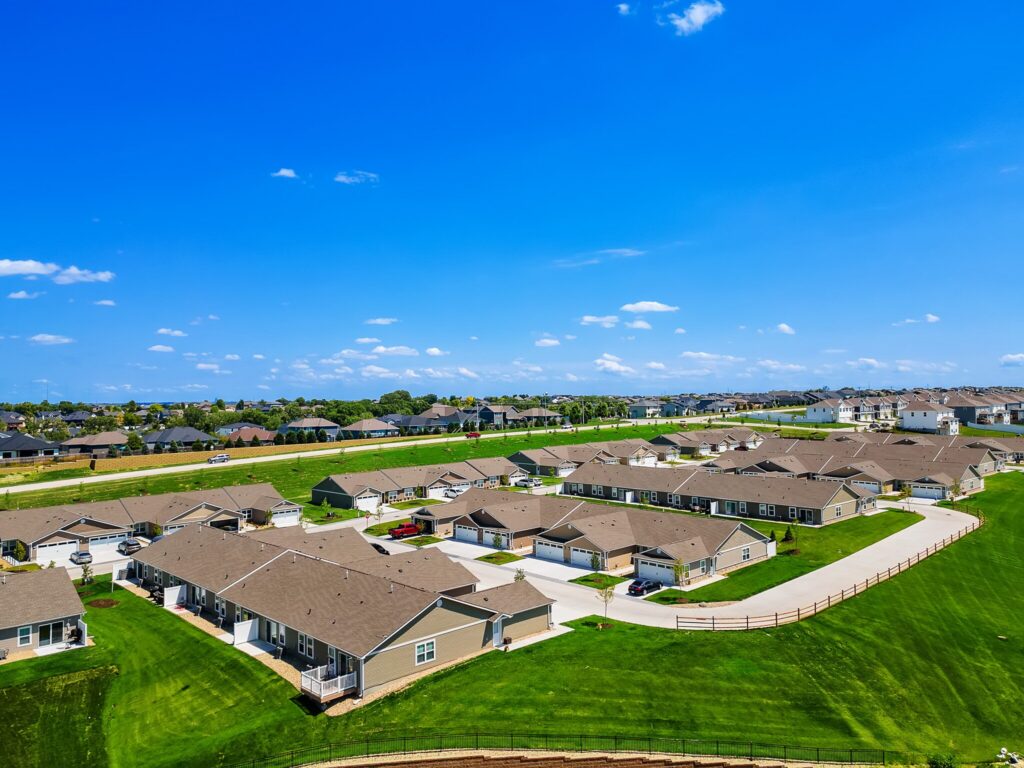 A suburban neighborhood with rows of single-story houses, neatly trimmed lawns, driveways, and clear blue sky overhead.