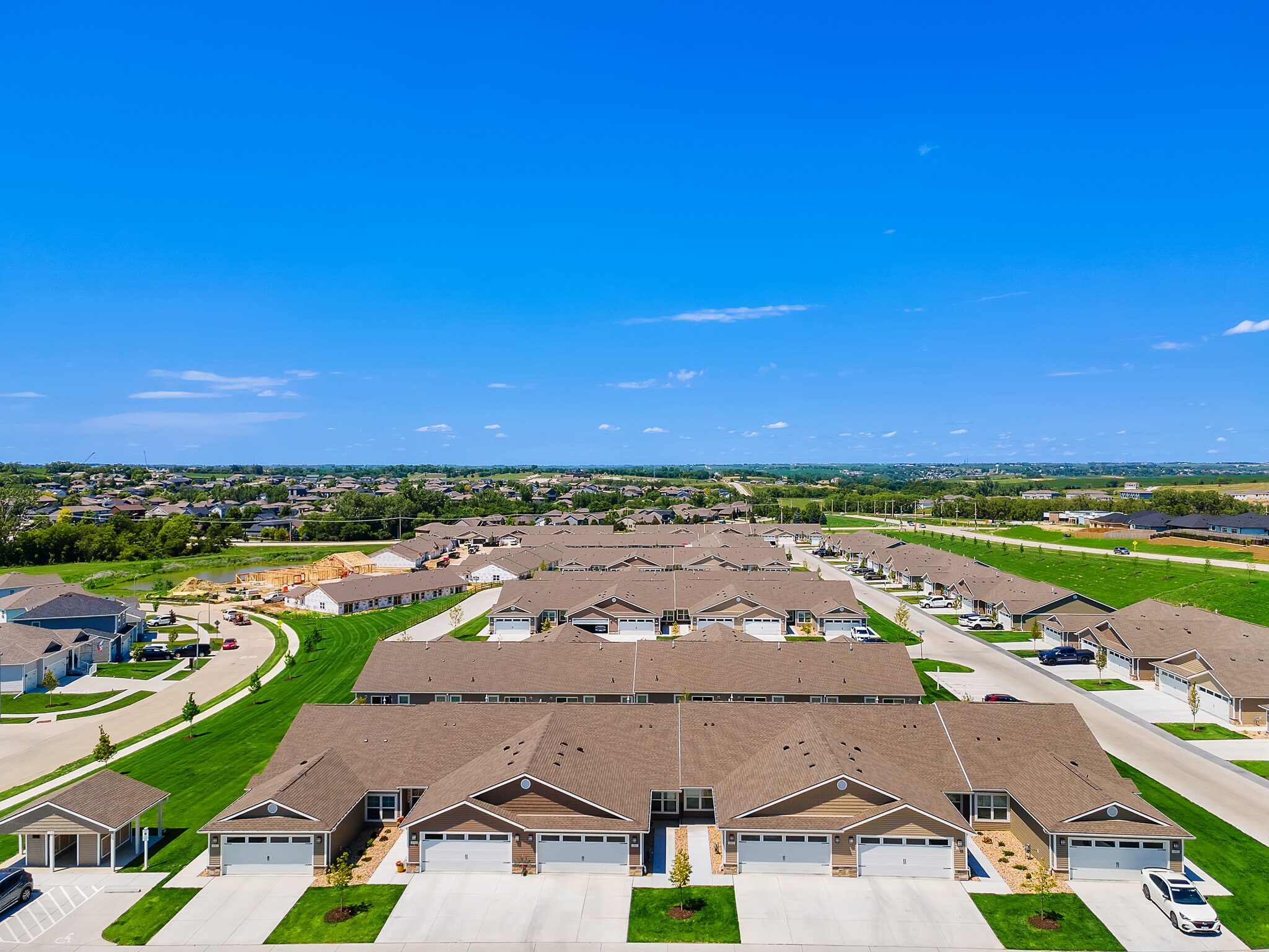 Aerial view of a suburban neighborhood with rows of houses, green lawns, driveways, and clear blue skies.