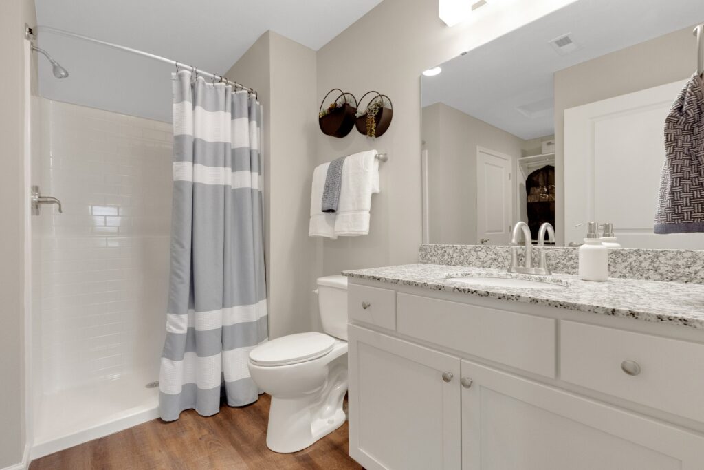 Modern bathroom with a shower, striped curtain, toilet, granite countertop, towels, and wall decor on light-colored walls and wood flooring.