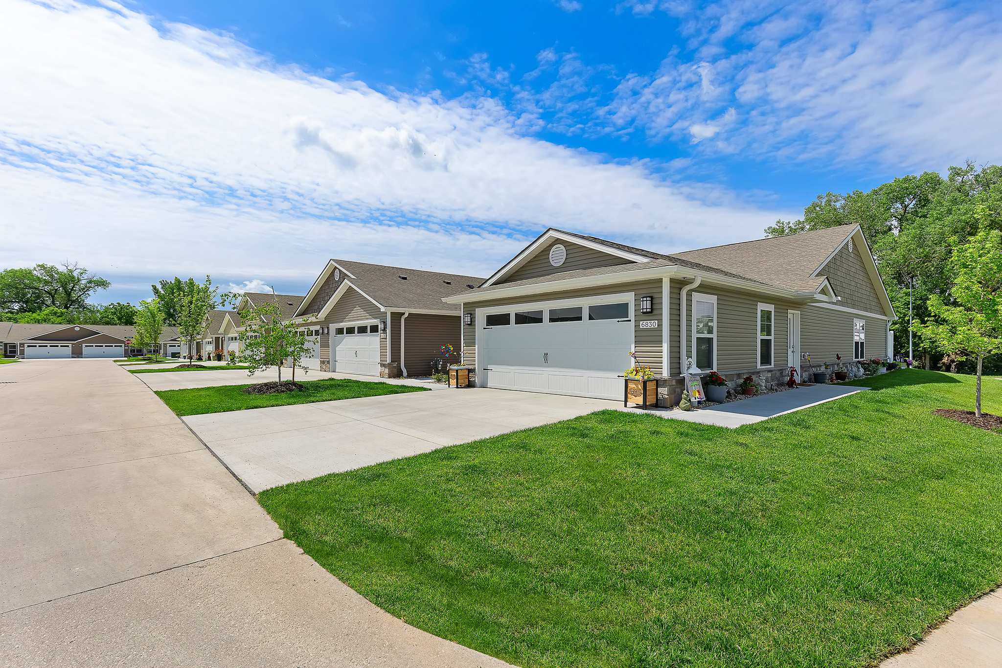Row of single-story suburban houses with attached garages, concrete driveways, and well-kept lawns under a partly cloudy sky.