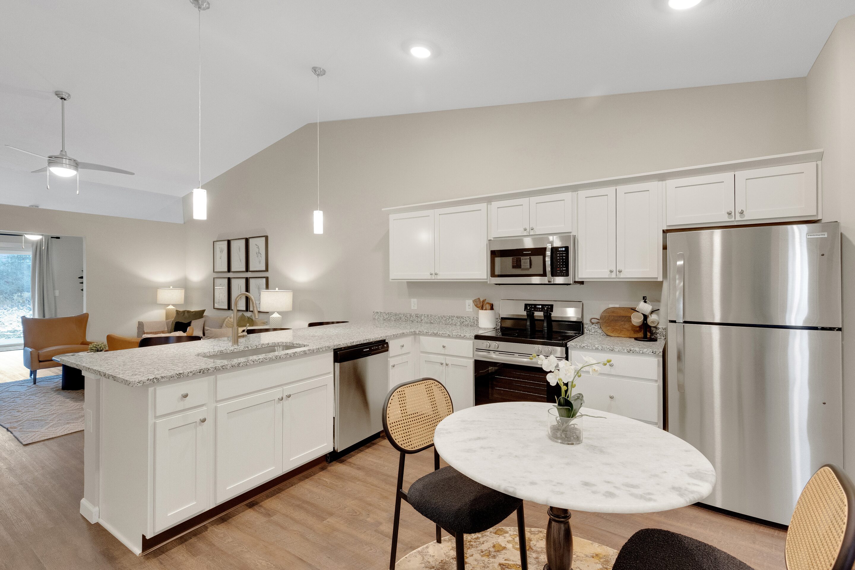 Modern kitchen with white cabinets, stainless steel appliances, granite countertops, a small round dining table, and an adjacent living area with seating.
