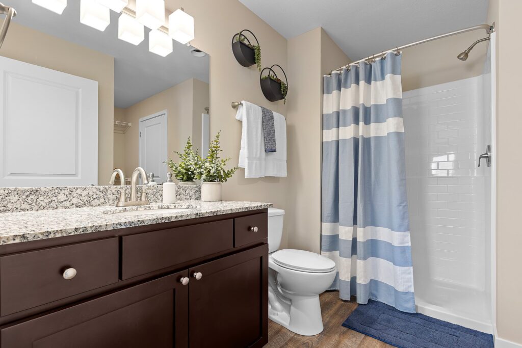 Modern bathroom with granite countertop, dark wood vanity, potted plant, towel rack, toilet, blue and white shower curtain, and wooden floor.