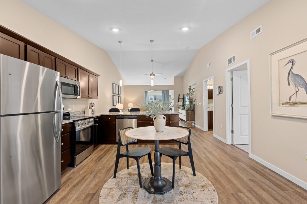 Modern kitchen and dining area with stainless steel appliances, dark wood cabinets, round table with two chairs, and artwork of a bird on the wall.