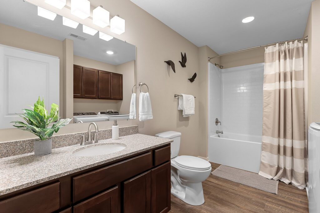 Modern bathroom with brown cabinets, granite countertop, white toilet, striped shower curtain, wall art, and potted plant on the sink.