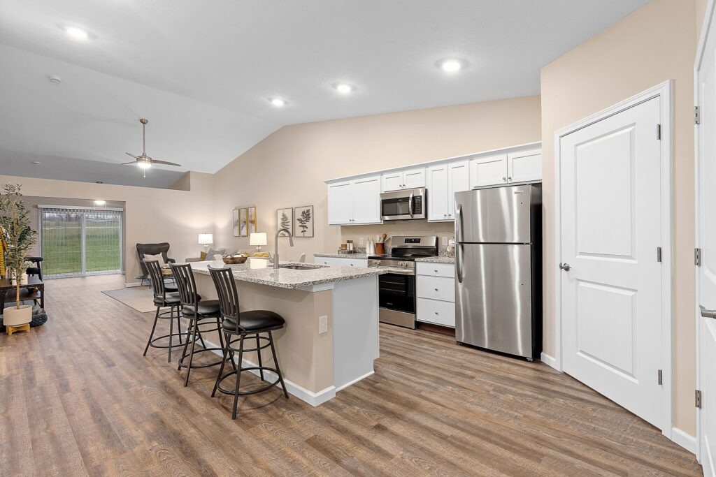 Modern open-concept kitchen and living area with white cabinets, stainless steel appliances, island seating, wood flooring, and neutral decor.