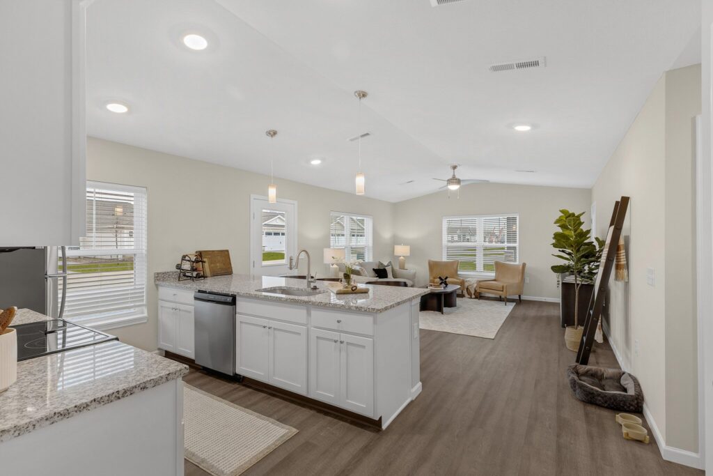 Open-concept kitchen and living room with white cabinets, granite countertops, wood flooring, neutral walls, and large windows letting in natural light.