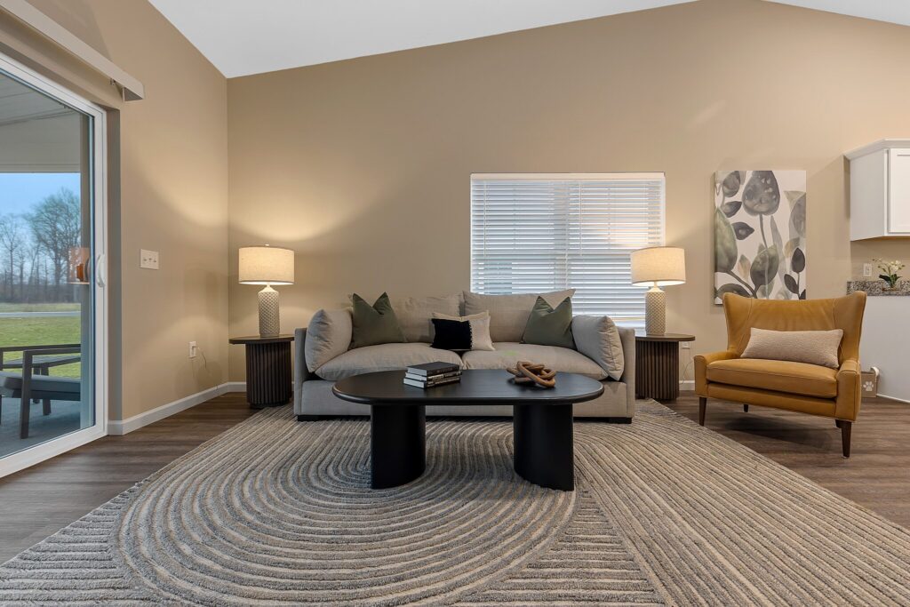 Modern living room with a gray sofa, black coffee table, two lamps, a yellow armchair, and a large window, featuring neutral colors and a circular patterned rug.