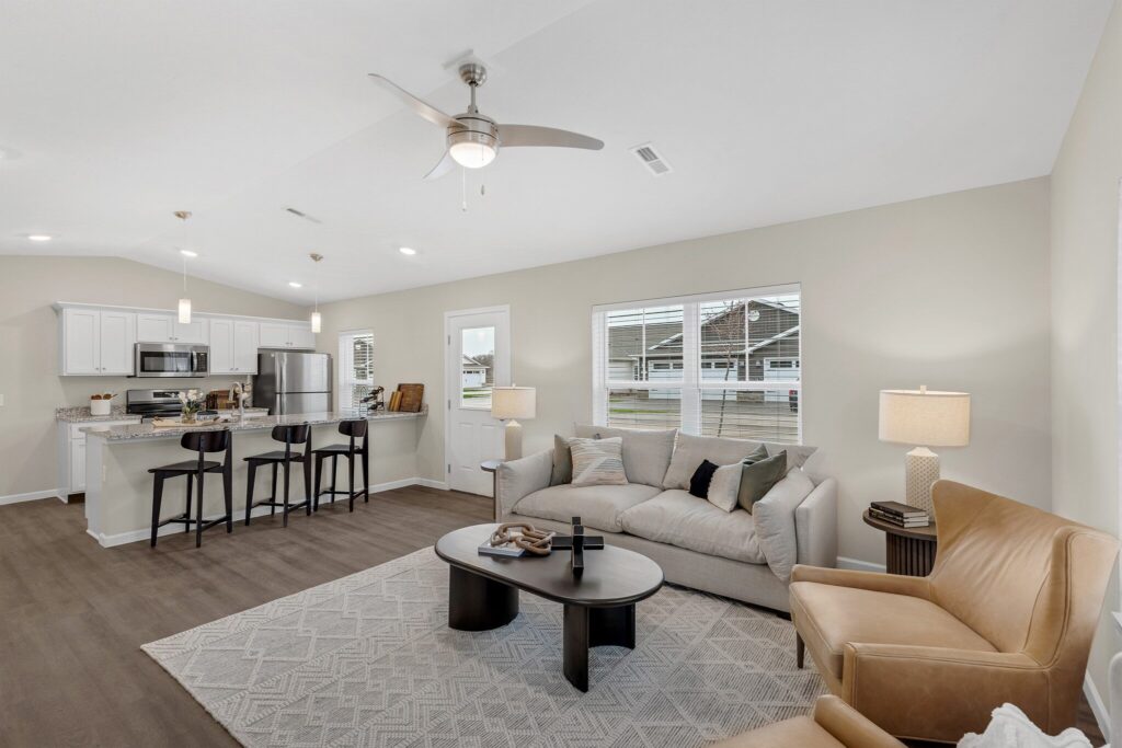 Open-concept living room and kitchen with neutral decor, modern furniture, a ceiling fan, and natural light from multiple windows.