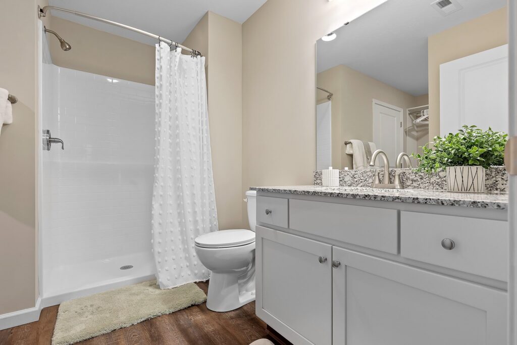 Modern bathroom with a walk-in shower, white vanity with granite countertop, toilet, potted plant, and wood-style flooring.