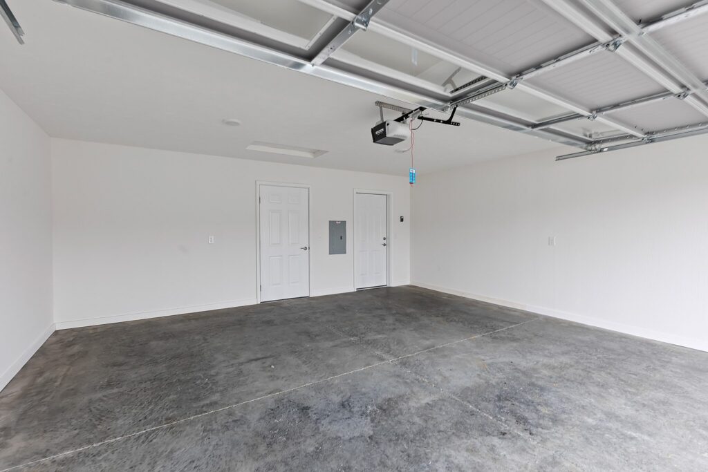 Empty two-car garage with concrete floor, white walls, two closed doors, and a ceiling-mounted garage door opener.