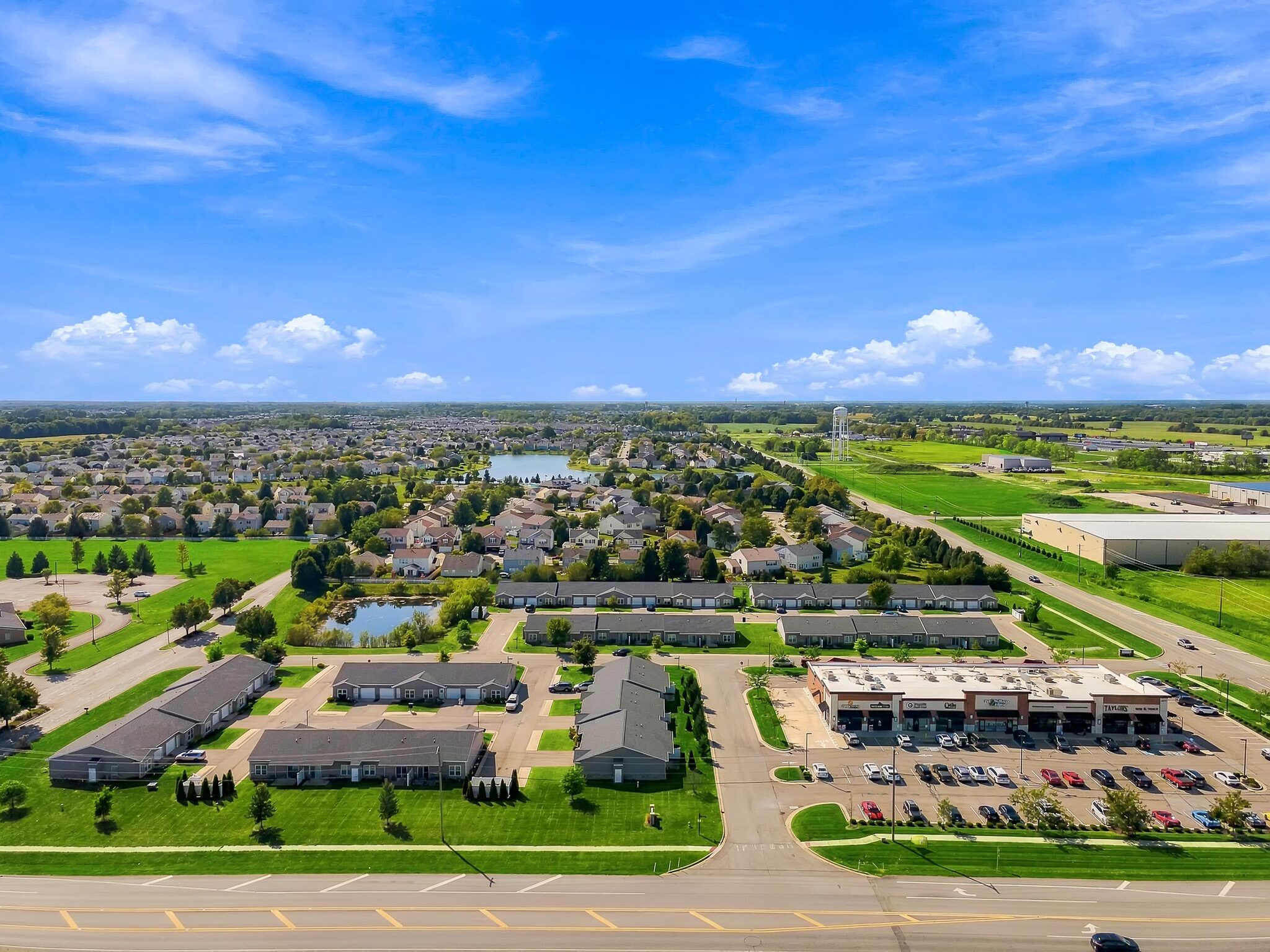 Aerial view of a residential neighborhood, apartment complexes, and a retail strip center with a parking lot.