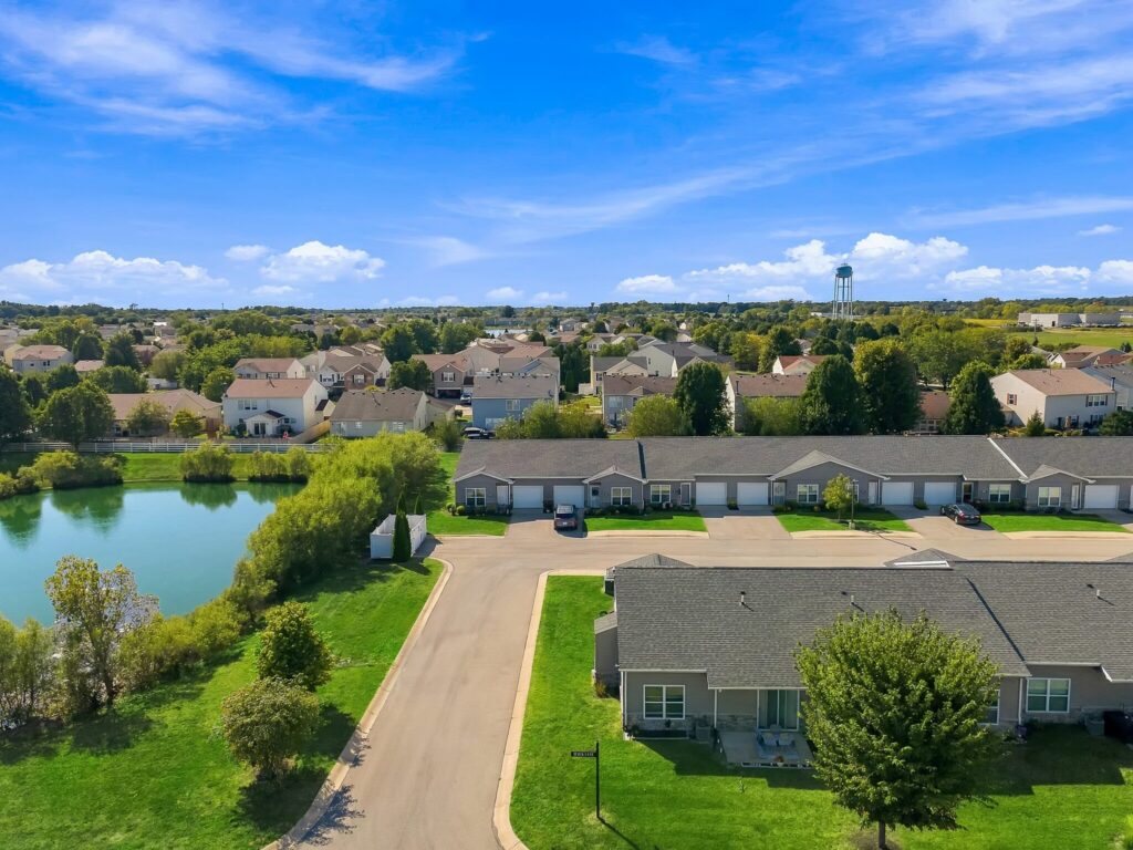 Aerial view of a residential neighborhood with suburban homes, a small pond, and a water tower in the distance.
